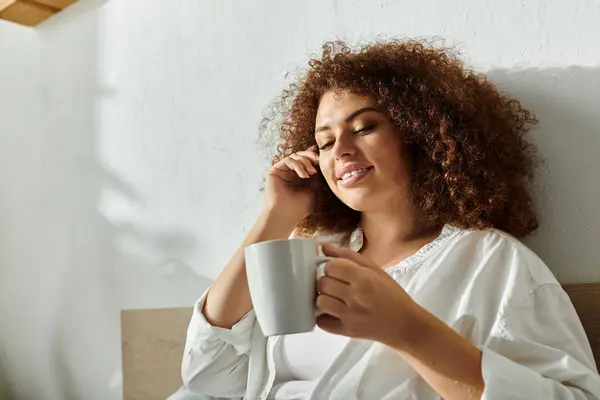 A relaxed woman smiles warmly as she talks on the phone, enjoying her drink. — Stock Photo