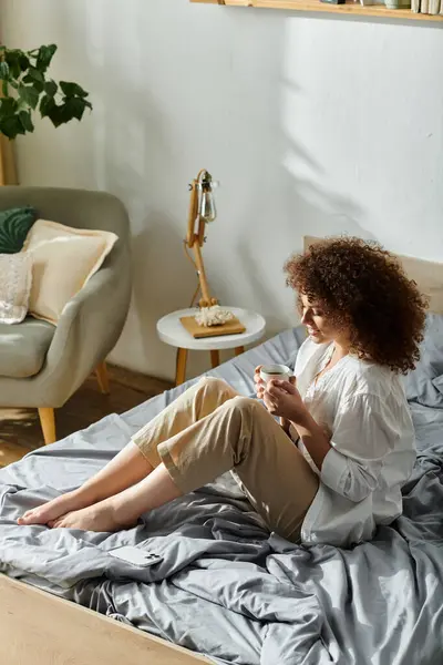 A woman sits comfortably on a bed while absorbed in a personal moment, surrounded by tranquility. — Stock Photo