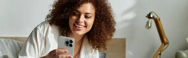 She smiles brightly as she interacts with her smartphone in a warm, inviting room. — Stock Photo
