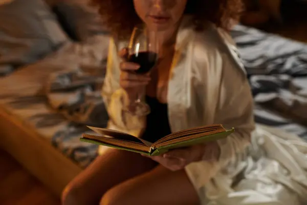 Embracing tranquility, a woman reads a book with a glass of red wine in hand in her bedroom. — Stock Photo