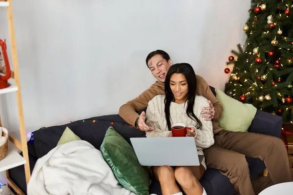 A loving couple relaxes on a couch, sharing holiday moments while viewing their laptop. — Stock Photo