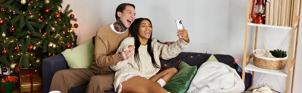 A happy couple cuddles on the couch, capturing festive moments together during Christmas. — Stock Photo