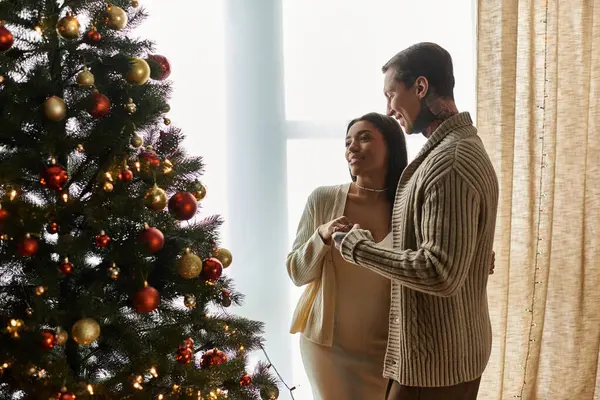 A couple shares a heartfelt moment by their beautifully decorated Christmas tree at home. — Stock Photo
