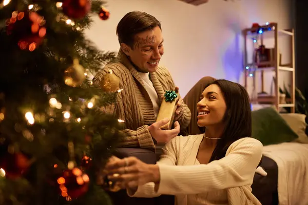 A loving couple exchanges gifts and shares smiles while celebrating Christmas at home. — Stock Photo