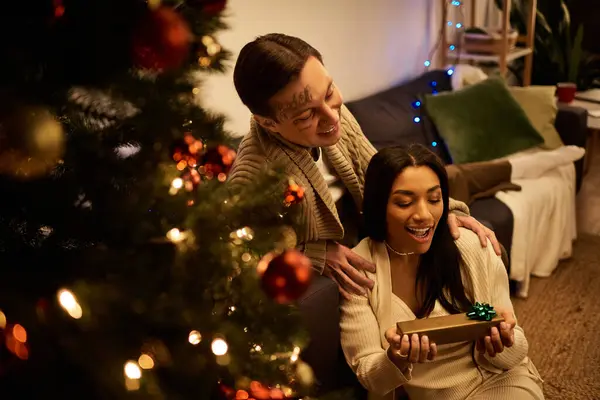 A joyful couple enjoys a loving Christmas moment, exchanging gifts by the decorated tree. — Stock Photo