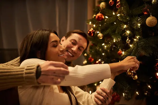 Una coppia felice condivide un momento gioioso mentre appende ornamenti sul loro albero di Natale a casa. — Foto stock