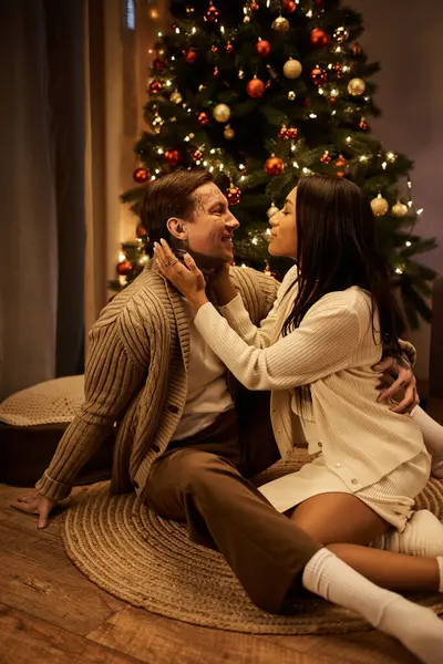A couple joyfully shares a tender moment by their beautifully decorated Christmas tree at home. — Stock Photo