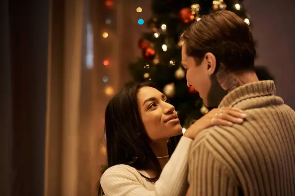 A couple embraces lovingly under the soft glow of Christmas lights at home, radiating warmth. — Stock Photo