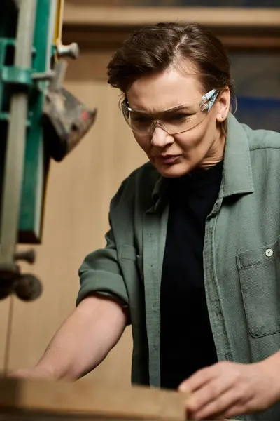 A focused carpenter works diligently with wood, showcasing craftsmanship in her well-lit workshop. — Stock Photo