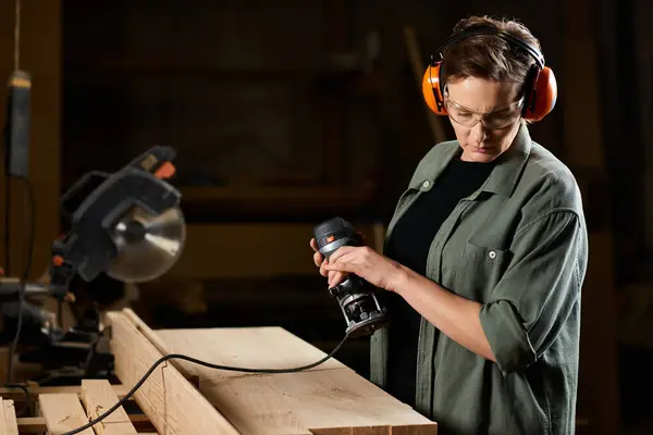 A skilled carpenter focuses intently while using power tools on a wooden project in her workshop space. — Stock Photo