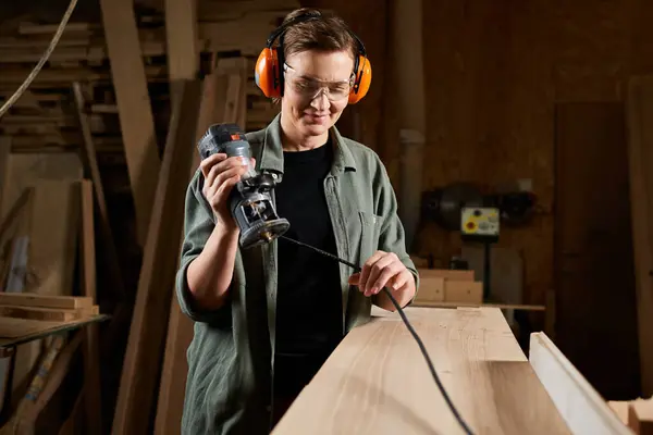 A skilled carpenter uses a router to craft wood with precision in her vibrant workshop. — Stock Photo