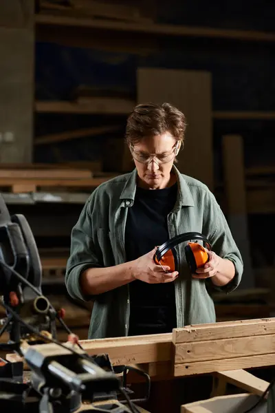 A skilled carpenter checks her safety equipment while working in a busy workshop filled with wood. — Stock Photo