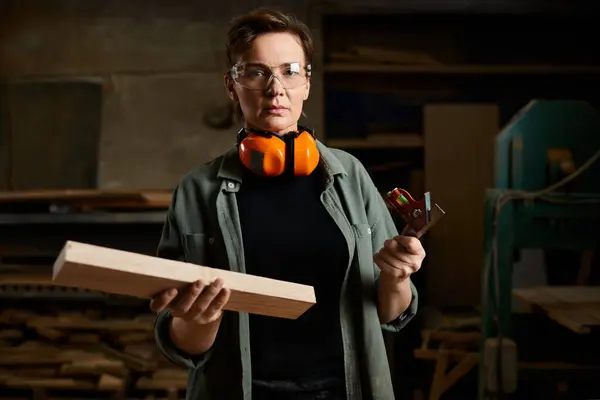 Una falegname donna lavora diligentemente con il legno, misurando e preparando materiali nel suo laboratorio. — Foto stock