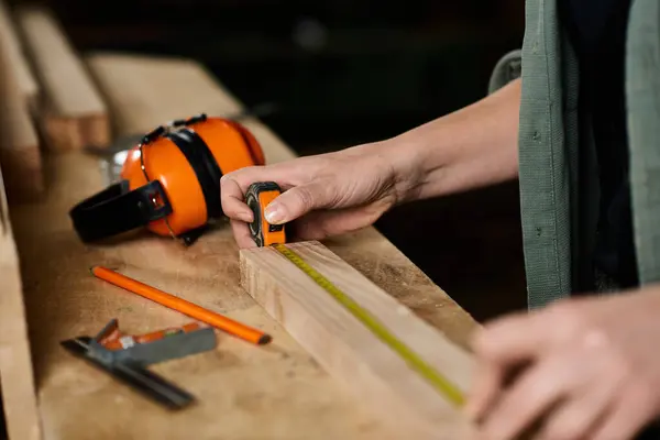 A skilled carpenter carefully measures wood with a tape measure in a workshop filled with tools and creativity. — Stock Photo