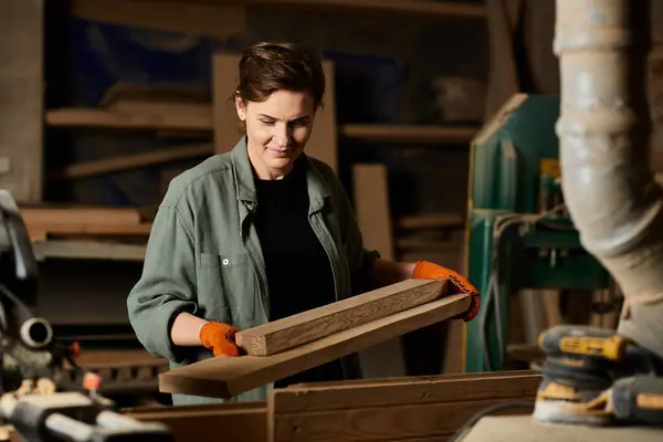 A skilled carpenter, wearing gloves, focuses on crafting wood pieces in her vibrant workshop filled with tools. — Foto stock