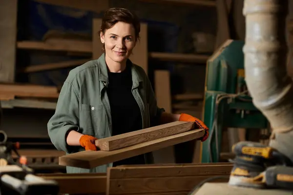 Una mujer talentosa da forma expertamente a la madera mientras usa guantes, mostrando su artesanía en un taller ocupado. - foto de stock