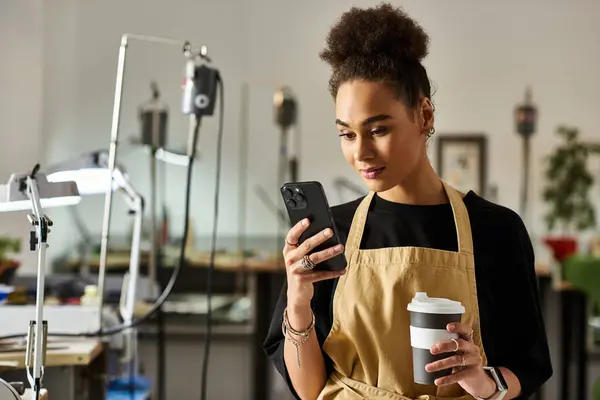 A woman admires her phone while holding a cup of coffee in an artistic studio setting. — Stock Photo