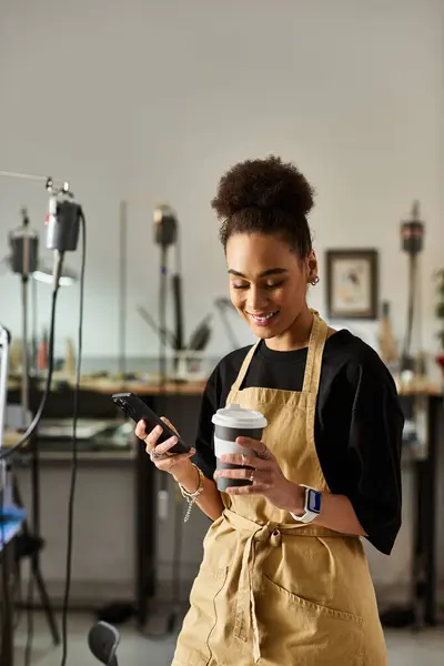 Une femme joyeuse aux cheveux coiffés tient une tasse de café et un téléphone dans un espace de travail animé. — Photo de stock