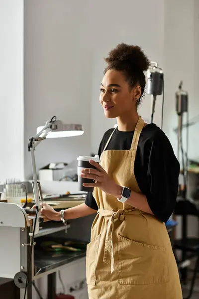 Une femme talentueuse conçoit des bijoux exquis tout en profitant d'une boisson chaude dans son studio. — Photo de stock