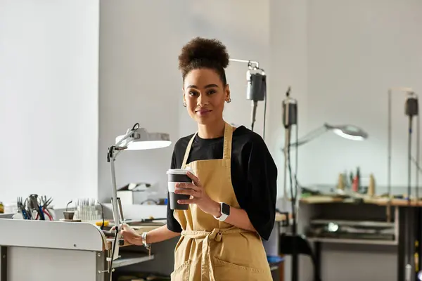 Eine erfahrene Kunsthandwerkerin lächelt, während sie ihren Kaffee in einem lebendigen Atelier genießt, das mit Werkzeugen gefüllt ist. — Stockfoto