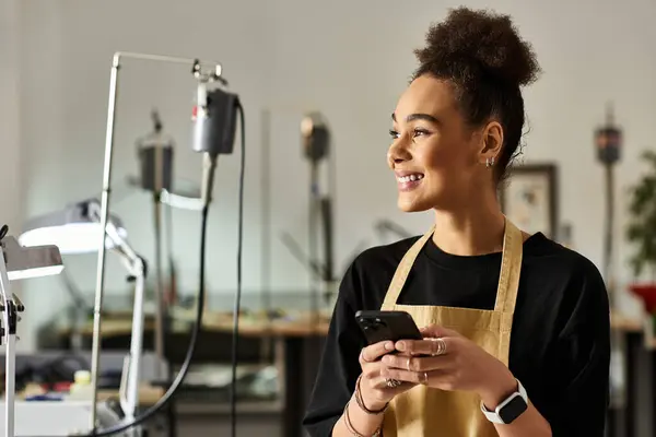 A woman smiles brightly while holding her phone, surrounded by tools and creativity. — Stock Photo
