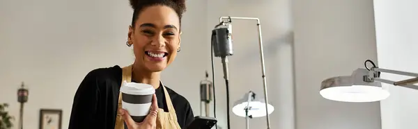 A cheerful woman holding a coffee cup, smiling brightly while enjoying her time in a studio. — Stock Photo