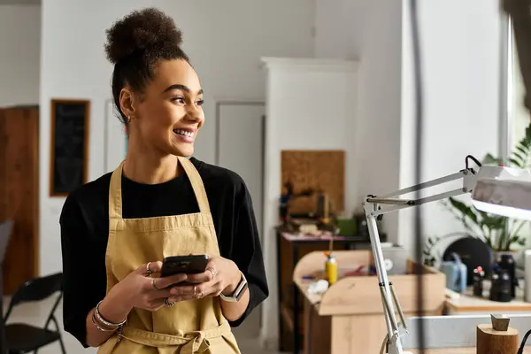 Une femme joyeuse s'engage avec son téléphone, entourée d'un espace de travail chaleureux et invitant. — Photo de stock