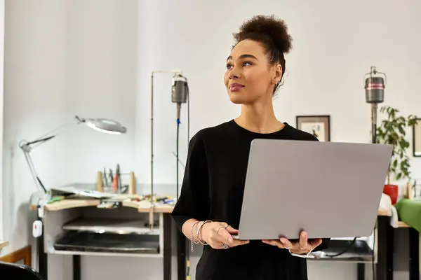 A woman stands proudly in her creative studio, holding a laptop while surrounded by art supplies. — Stock Photo