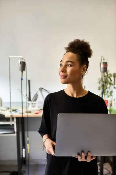 The beautiful woman holds a laptop while contemplating her artistic designs in a vibrant workspace. — Stock Photo
