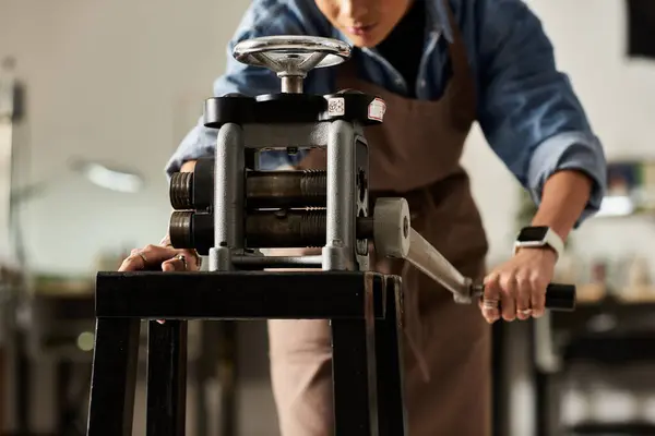 A focused craftsperson carefully rolls metal through a press, creating intricate jewelry pieces. — Stock Photo