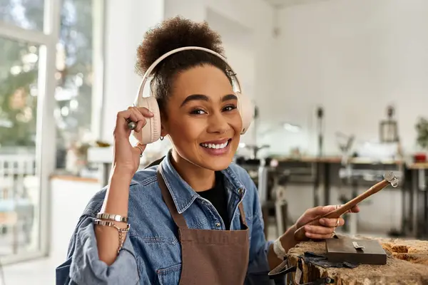 A skilled artisan smiles while creating stunning jewelry, wearing headphones in a bright workspace. — Stock Photo