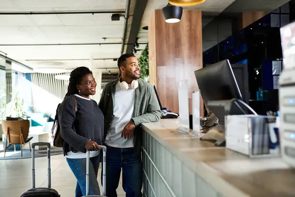 Una joven pareja afroamericana sonríe junta en el vestíbulo de un hotel mientras se prepara para sus vacaciones. - foto de stock
