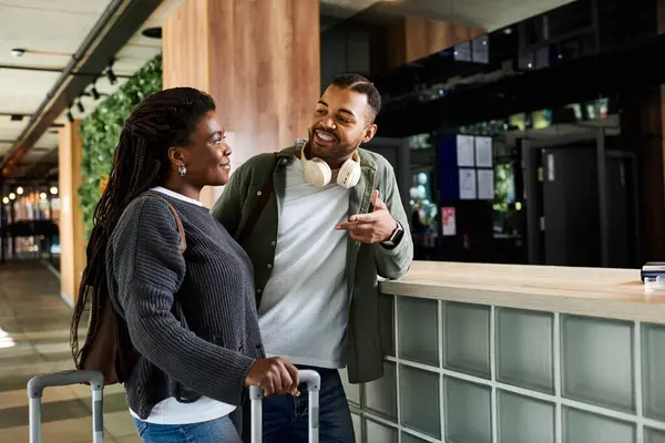 Una joven pareja afroamericana comparte una sonrisa mientras se registra en su hotel, listo para unas vacaciones. - foto de stock