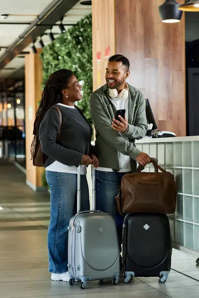 A joyful young couple with luggage smiles at each other in a stylish hotel lobby, ready for adventure. — Stock Photo