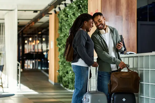 Ein fröhliches junges Paar steht an der Rezeption der Hotellobby und freut sich darauf, gemeinsam den Urlaub zu beginnen.. — Stockfoto
