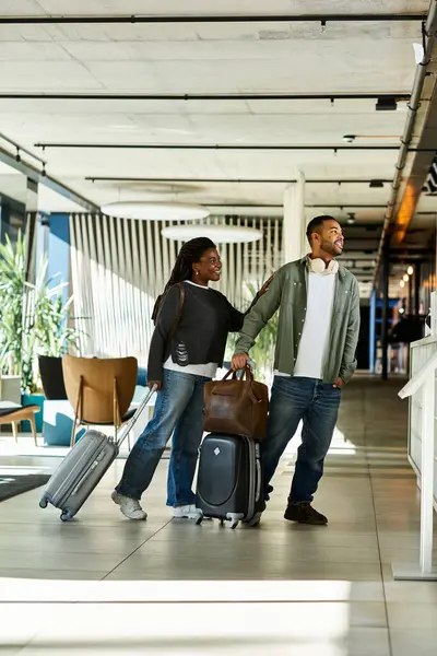 Ein fröhliches junges Paar mit Gepäck teilt die Aufregung in einer modernen Hotellobby, bereit für die Urlaubsreise. — Stockfoto