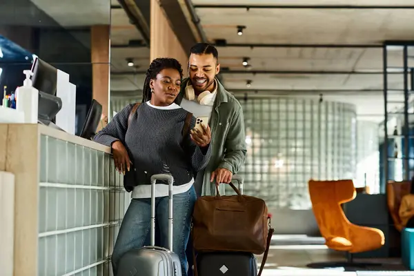Ein junges afroamerikanisches Paar genießt seinen Urlaub und checkt in einer stilvollen Hotellobby mit Gepäck ein. — Stockfoto