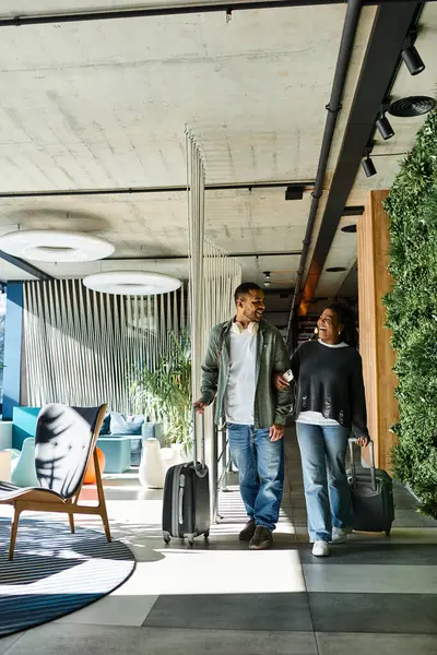 A young couple joyfully navigates a modern hotel lobby, ready for their vacation adventure. — Stock Photo