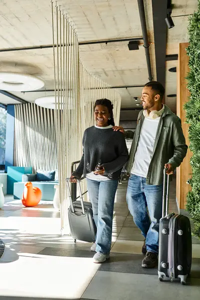 A happy young couple walks through a modern hotel lobby, carrying their luggage and preparing for an exciting getaway. — Stock Photo
