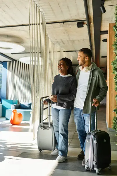 A joyful couple holds luggage while entering the hotel lobby, ready to enjoy their holiday adventure. — Stock Photo