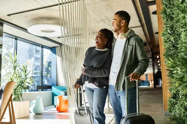 A young couple laughs happily while navigating through a hotel lobby, ready for their vacation adventure. — Stock Photo