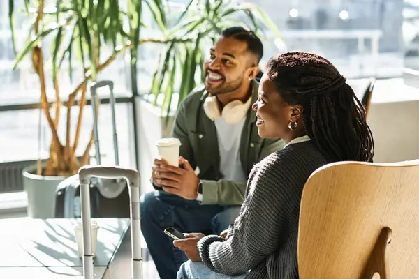 A cheerful young couple relaxes in a stylish hotel lobby, sharing smiles and savoring their vacation moment. — Stock Photo