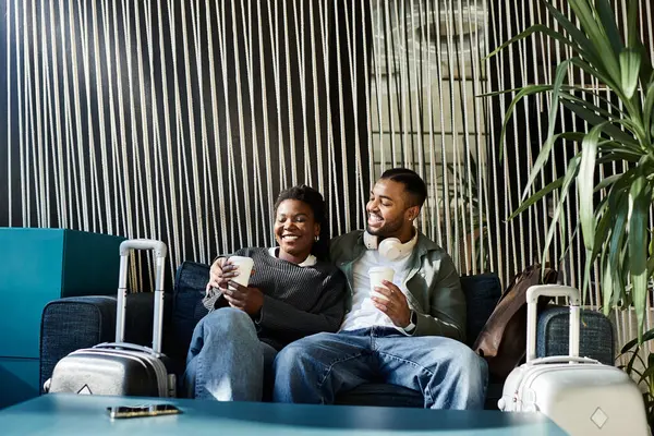 Um jovem casal alegre relaxa em um lobby moderno do hotel, bebendo bebidas e compartilhando sorrisos durante suas férias. — Fotografia de Stock