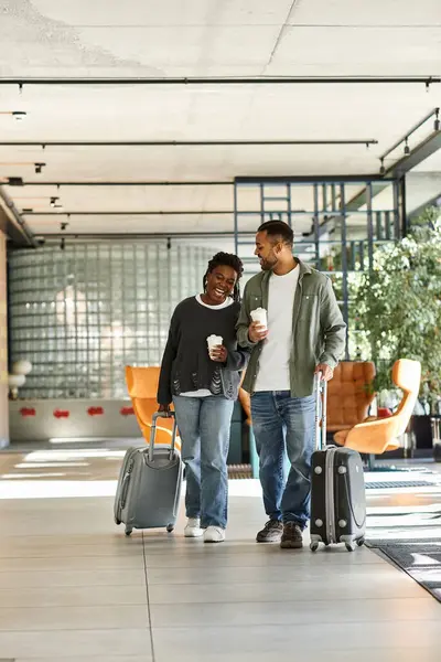 Una giovane coppia cammina mano nella mano attraverso un'elegante hall dell'hotel, sorseggiando un caffè e godendo il loro viaggio. — Foto stock