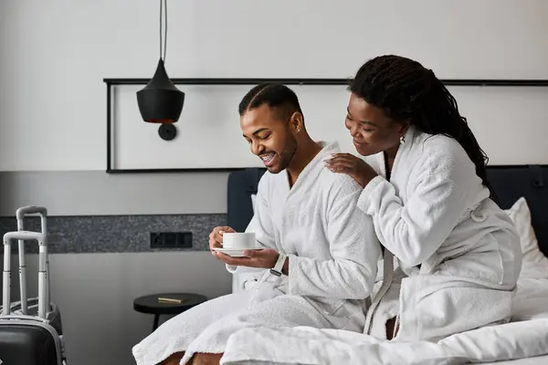 A loving couple shares a joyful moment in their hotel room, savoring coffee while relaxing in robes. — Stock Photo