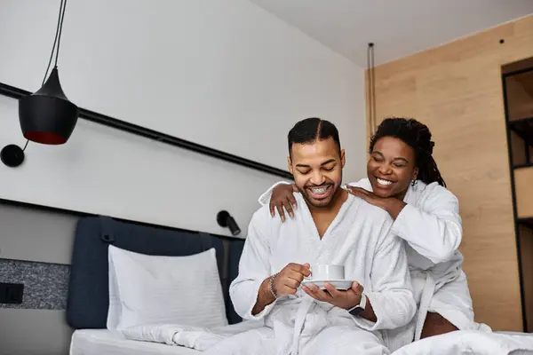 Una giovane coppia gioiosa condivide un momento tenero nella loro camera d'albergo, avvolta in accappatoi accoglienti durante le vacanze. — Foto stock