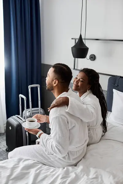 A young couple relaxes and shares joyful moments in their hotel room, wrapped in plush robes. — Stock Photo