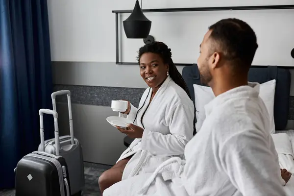 A cheerful young couple shares a romantic morning, sipping coffee while relaxing in their hotel room. — Stock Photo