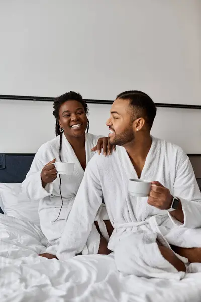 Un jeune couple joyeux partage des moments intimes autour d'un café, enveloppé dans des robes confortables pendant leur escapade romantique. — Photo de stock