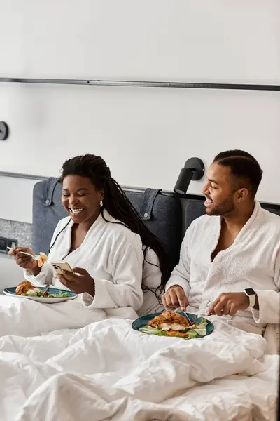 Una joven pareja comparte risas y una deliciosa comida envuelta en túnicas acogedoras, creando recuerdos inolvidables. - foto de stock